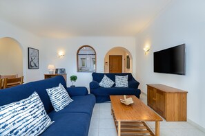 Ein modernes Wohnzimmer mit einer Sofagarnitur, einem Holztisch, einem an der Wand montierten Fernseher und einer Holzkommode.