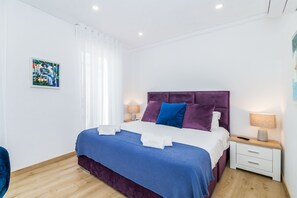 A modern bedroom with a bed, nightstands, and a painting on the wall. - Vista Bonita | Dowtown | Family (Lagos)