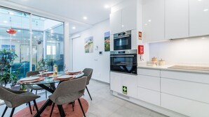 Una cucina moderna con mobili bianchi, forno integrato e zona pranzo in vetro con sedie grigie.