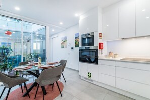 A modern kitchen with white cabinets, a built-in oven, and a glass dining area with grey chairs. - Vista Bonita | Dowtown | Family (Lagos)