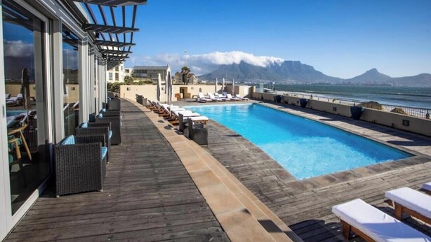 A poolside area with lounge chairs, a wooden deck, and a view of the sea and mountains. - Luxurious Accessible Apartment With Ocean Views in Kaapstad (Cape Town)