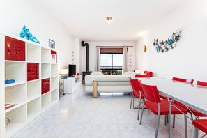 A modern room with a sofa, dining table, red chairs, a TV, and a window with a view. - Lagos Sea View | Near the City Center (Lagos)