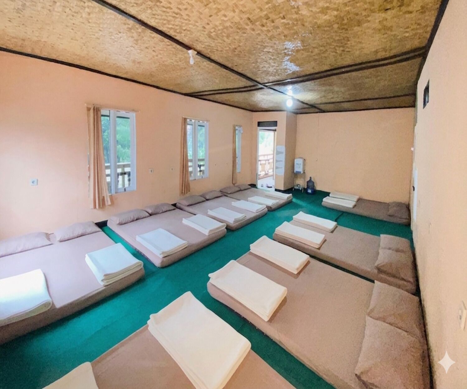 Ein Zimmer mit mehreren reihenweise angeordneten Betten, einem grünen Teppich und einer Holzziel.