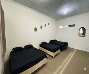 Ein Zimmer mit drei Betten, einem kleinen Fenster und einem Spiegel an der Wand.