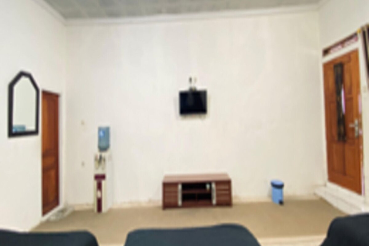 Ein Zimmer mit zwei Betten, einem an der Wand befestigten Fernseher, einer Holztür und einem kleinen Schrank.