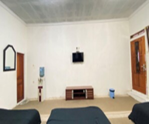 Ein Zimmer mit zwei Betten, einem an der Wand befestigten Fernseher, einer Holztür und einem kleinen Schrank.