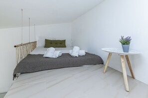 A bedroom with a bed, pillows, a bedside table with a plant, and a small round table. - Chilling Studio in Lagos (Lagos)