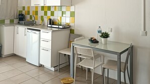 A compact kitchen with white cabinets, a tiled backsplash, a small dining table with chairs, and a hanging pendant light. - Chilling Studio in Lagos (Lagos)