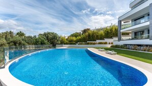A modern swimming pool with a glass balustrade, surrounded by a well-maintained lawn and a contemporary building. - Ria Terrace House in Alvor (Alvor)