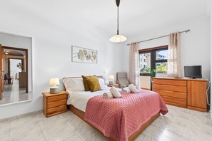 A bedroom with a bed, bedside tables, a TV, a dresser, and a window with curtains. - Casa Oliveira 31 in Lagos (Lagos)