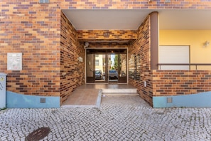 A building entrance with a brick facade, a tiled ground, and a visible door. - Casa Oliveira 31 in Lagos (Lagos)