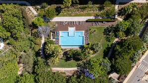 Vista aérea de un hotel con piscina central, rodeado de exuberante vegetación y un estacionamiento.