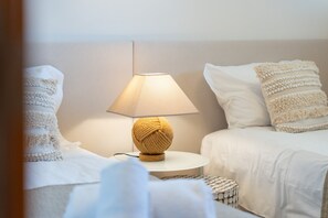 Un lit bien fait, recouvert d’une couverture blanche et agrémenté d’oreillers, une table ronde avec une lampe, et un mur au décor sobre.