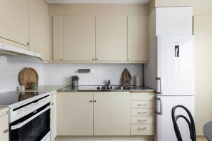 Una cocina compacta con estufa, horno, pileta y un refrigerador blanco.