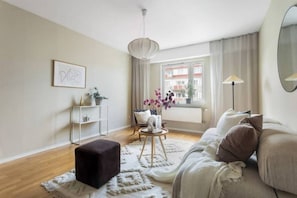 Un salon moderne avec un canapé, une petite table sur laquelle est posé un vase de fleurs, une lampe sur pied et une fenêtre avec des rideaux.