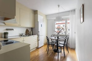 Une cuisine moderne avec des meubles blancs, une table à manger avec des chaises et une vue sur les immeubles par la fenêtre.