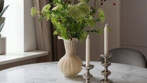 Un tavolo rotondo in marmo con un vaso bianco che contiene verdeggiante fogliame e bacche rosse, affiancato da due candelabri.