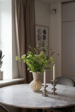 Un tavolo rotondo in marmo con un vaso bianco che contiene verdeggiante fogliame e bacche rosse, affiancato da due candelabri.