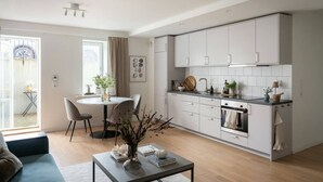 Una cucina moderna con mobili bianchi, una zona pranzo con un tavolo rotondo e sedie, e un soggiorno con un divano e un tavolino.
