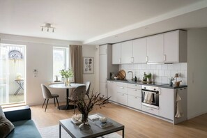 Een moderne keuken met witte kasten, een eethoek met een ronde tafel en stoelen, en een woonkamer met een bank en salontafel.