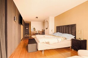 Ein modernes Schlafzimmer mit einem großen Bett, einem Nachttisch, einem Flachbildfernseher und einem kleinen Schreibtisch mit Stuhl.
