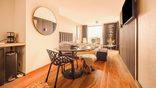 Une chambre d’hôtel moderne avec une table à manger ronde, un canapé, une télévision et un petit coin cuisine.