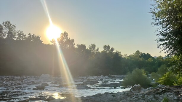 Une table à manger avec des assiettes et une baguette, deux chaises, et une vue sur une rivière au coucher du soleil.