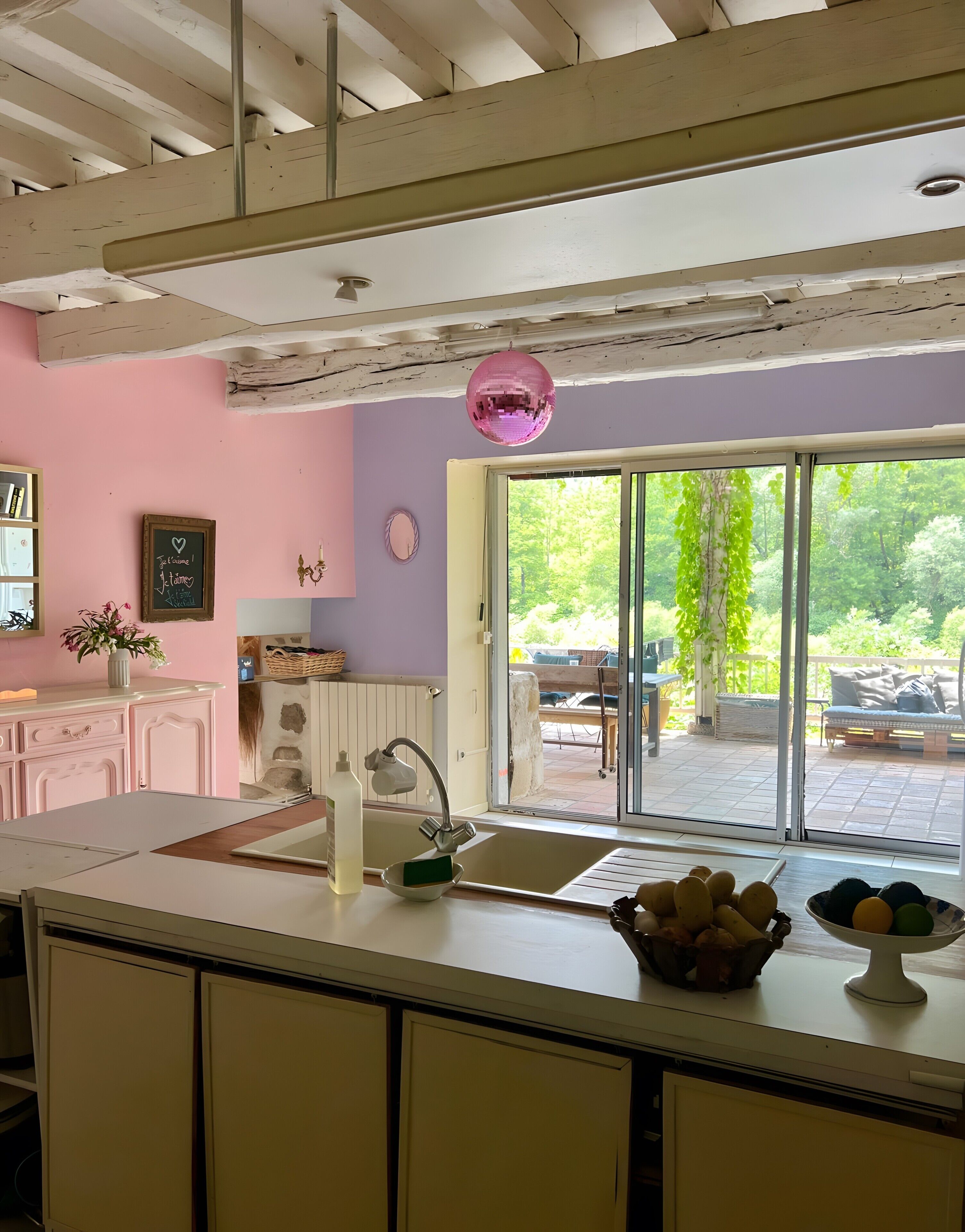 A kitchen with a large window, a pink disco ball, and a view of the outdoors.