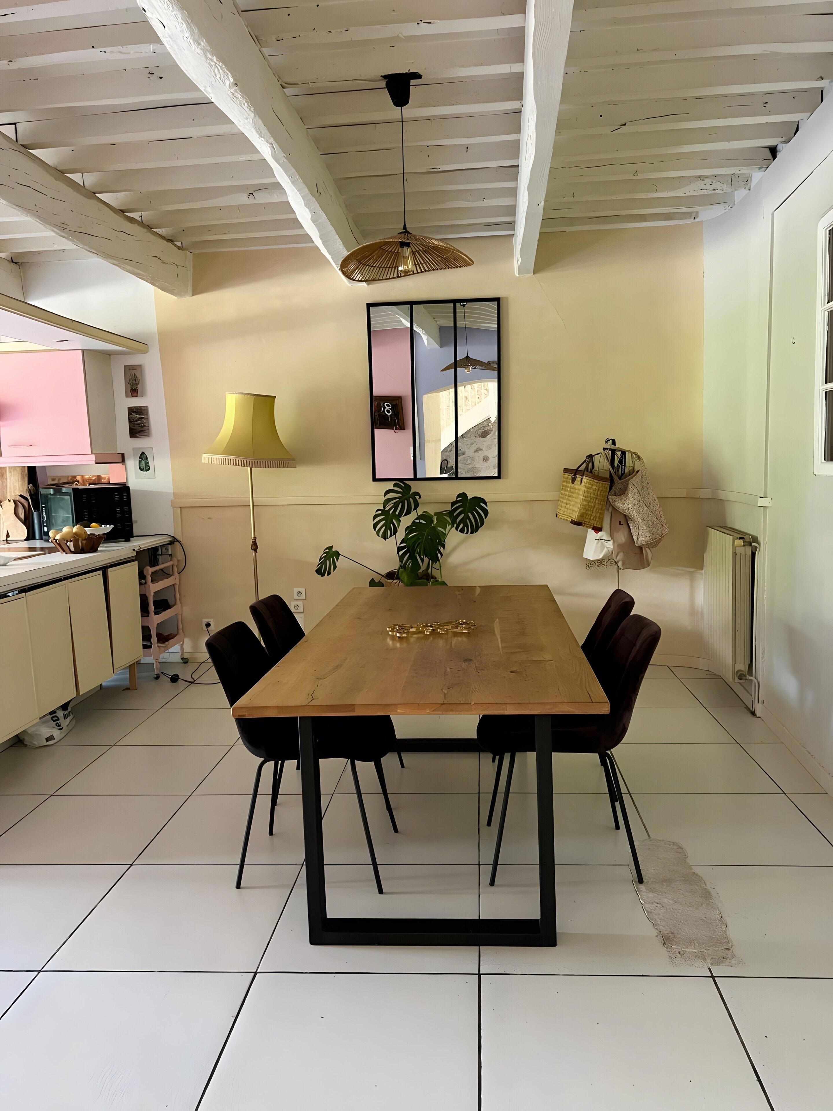 Een eethoek met een houten tafel, zwarte stoelen, een hanglamp, een potplant en een spiegel aan de muur.