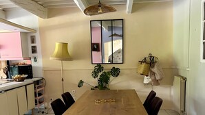 Un coin repas avec une table en bois, des chaises noires, un luminaire suspendu, une plante en pot et un miroir au mur.