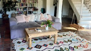 Un salon chaleureux avec un canapé, une table basse et une bibliothèque, un escalier et un tapis à motifs.