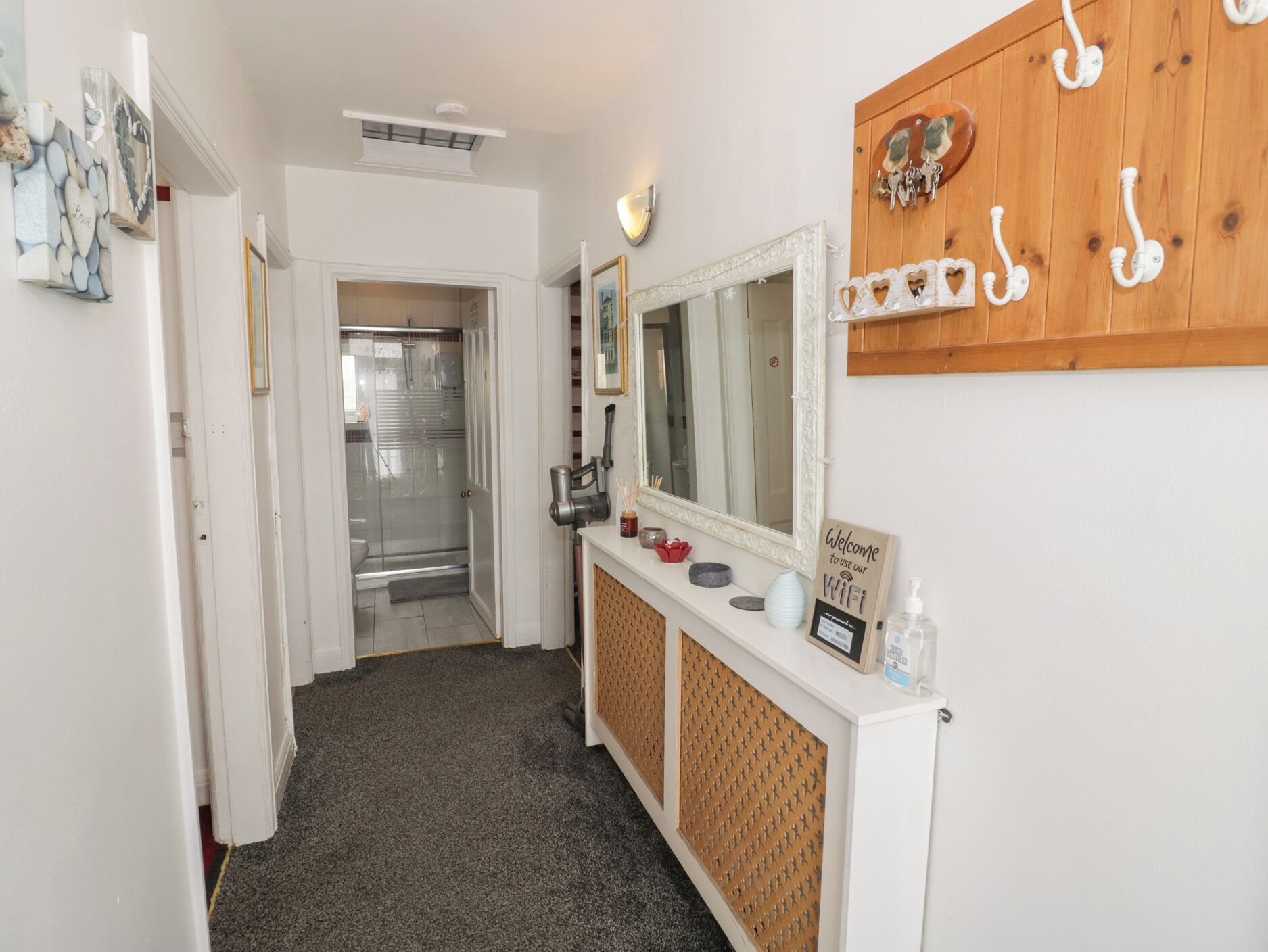 A hallway with a shower, a mirror, a vanity with toiletries, and a wall-mounted coat rack.