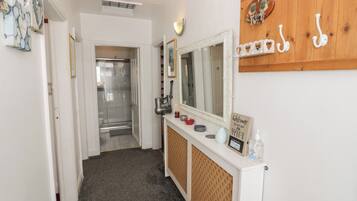 A hallway with a shower, a mirror, a vanity with toiletries, and a wall-mounted coat rack.