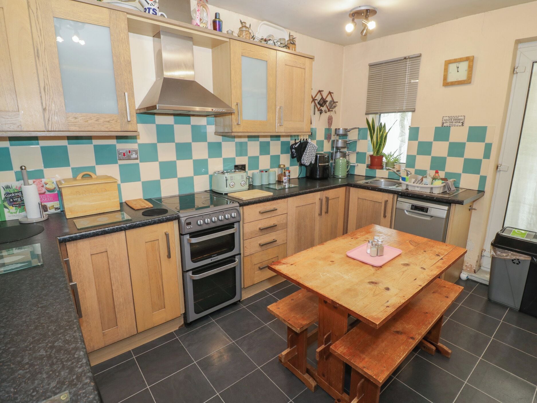 A kitchen with wooden cabinets, a stove, a sink, and a dining table with benches.