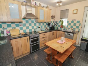 A kitchen with wooden cabinets, a stove, a sink, and a dining table with benches. - Mount Joy (Leicester)