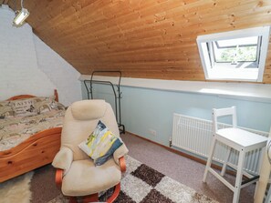 A room with a sloped ceiling, a bed with a patterned bedspread, a chair with a cushion, a radiator, and a window with a view. - Mount Joy (Leicester)
