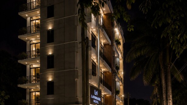 Een hotel met meerdere verdiepingen, balkons, een bord met de tekst Lanmark Hotel, en auto's die ervoor geparkeerd staan.