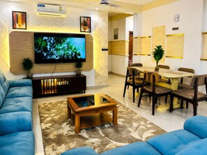 Ein modernes Wohnzimmer mit Flachbildfernseher, einer Couch, einem Couchtisch und einem Essbereich mit Stühlen und Tisch.