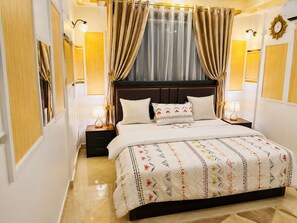 Ein Hotelzimmer mit einem großen Bett, zwei Nachttischen, einem Beistelltisch, einem Fenster mit Vorhängen und Wandlampen.