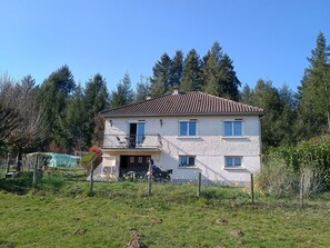 A two-story house with a balcony, surrounded by a fence and trees.