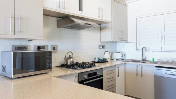 Una cocina moderna con electrodomésticos de acero inoxidable, armarios blancos y horno empotrado.