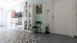 Un pasillo con piso estampado, una puerta blanca, una silla negra y una estantería con diversos objetos.