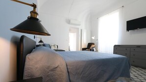 Un dormitorio con cama, escritorio, silla, cómoda y televisor montado en la pared.