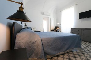 Une chambre à coucher comprenant un lit, un bureau, une chaise, une commode et un téléviseur fixé au mur.
