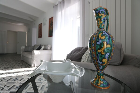 A room with a glass table, a colorful vase, a white sofa, and a patterned floor.