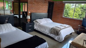 Ein Hotelzimmer mit zwei Betten, einem Fernseher, einem Schreibtisch und einem Fenster mit Blick auf Grünflächen.