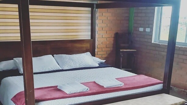 Ein Bett mit Baldachin und Holzrahmen, eine Sitzbank am Fußende, sowie eine Backsteinwand im Hintergrund.