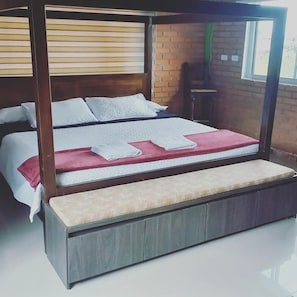 Un lit à baldaquin avec un cadre en bois, un banc au pied du lit et un mur en briques en arrière-plan.