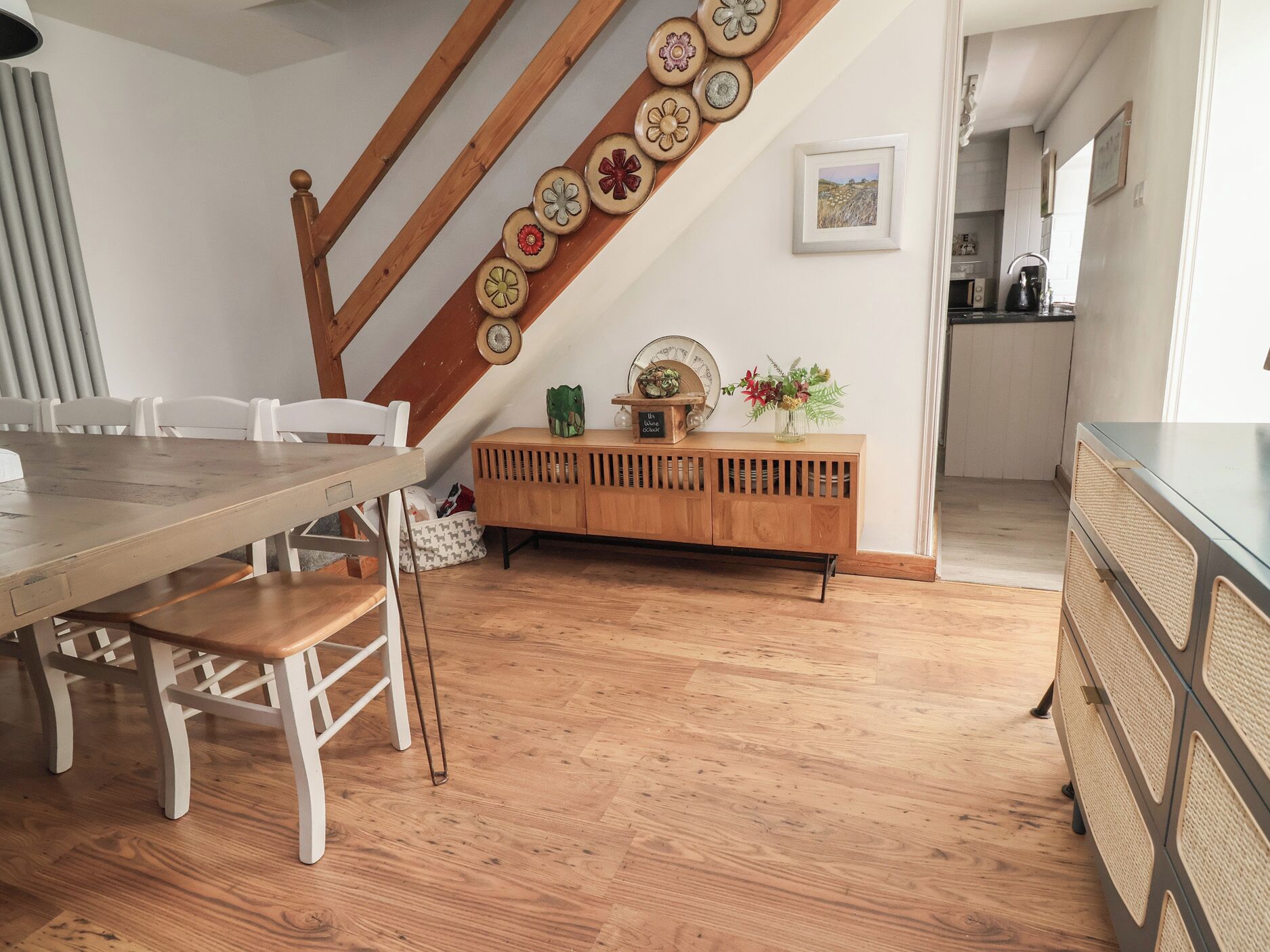 Un comedor con una mesa y sillas de madera, un mueble de madera con platos decorativos, y una escalera con baranda de madera.