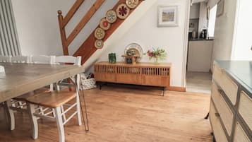 Un comedor con una mesa y sillas de madera, un mueble de madera con platos decorativos, y una escalera con baranda de madera.